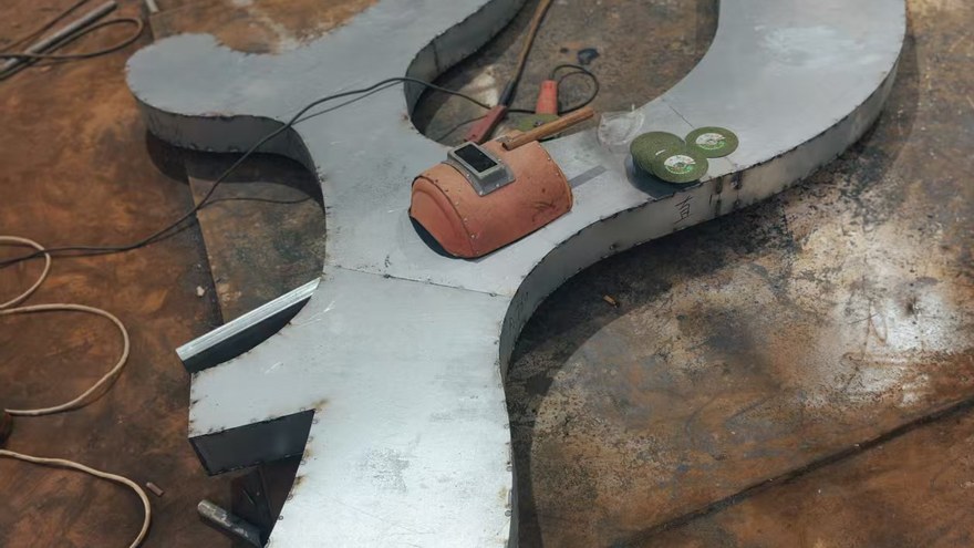 steel plate cut to shape on a workshop floor during playground part preparation खेल के मैदान के हिस्से की तैयारी के दौरान कार्यशाला के फर्श पर स्टील प्लेट को आकार देने के लिए काटा गया